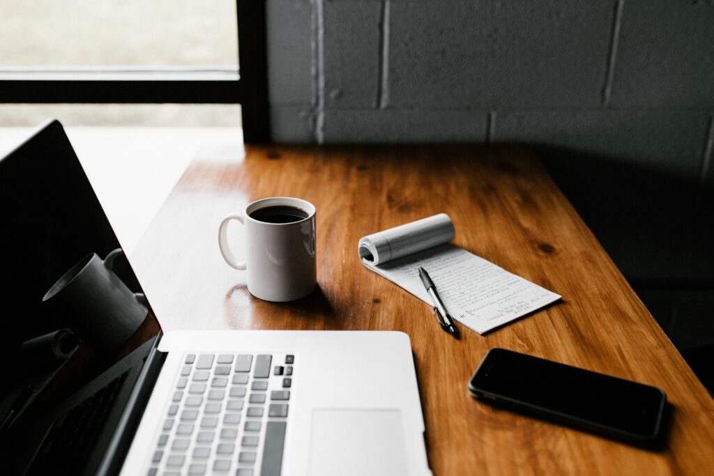 Laptop, coffee, phone, and notes on a desk for business contract drafting and review